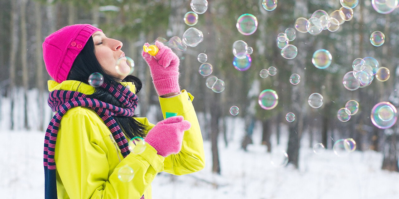 A woman blowing bubbles in winter sunlight, reflecting joy in suffering and gratitude even in unexpected seasons.