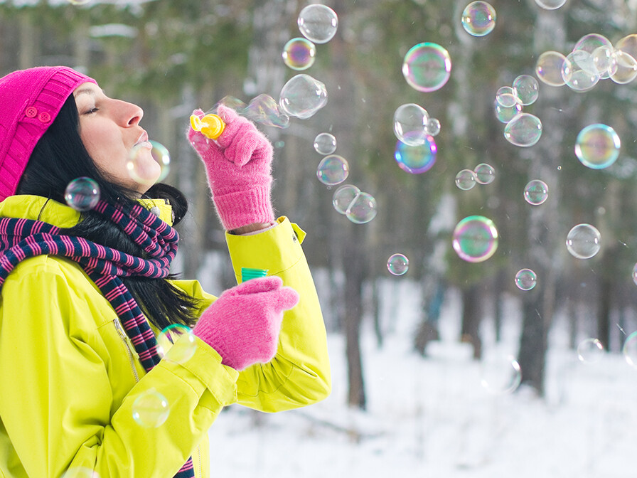 A woman blowing bubbles in winter sunlight, reflecting joy in suffering and gratitude even in unexpected seasons.