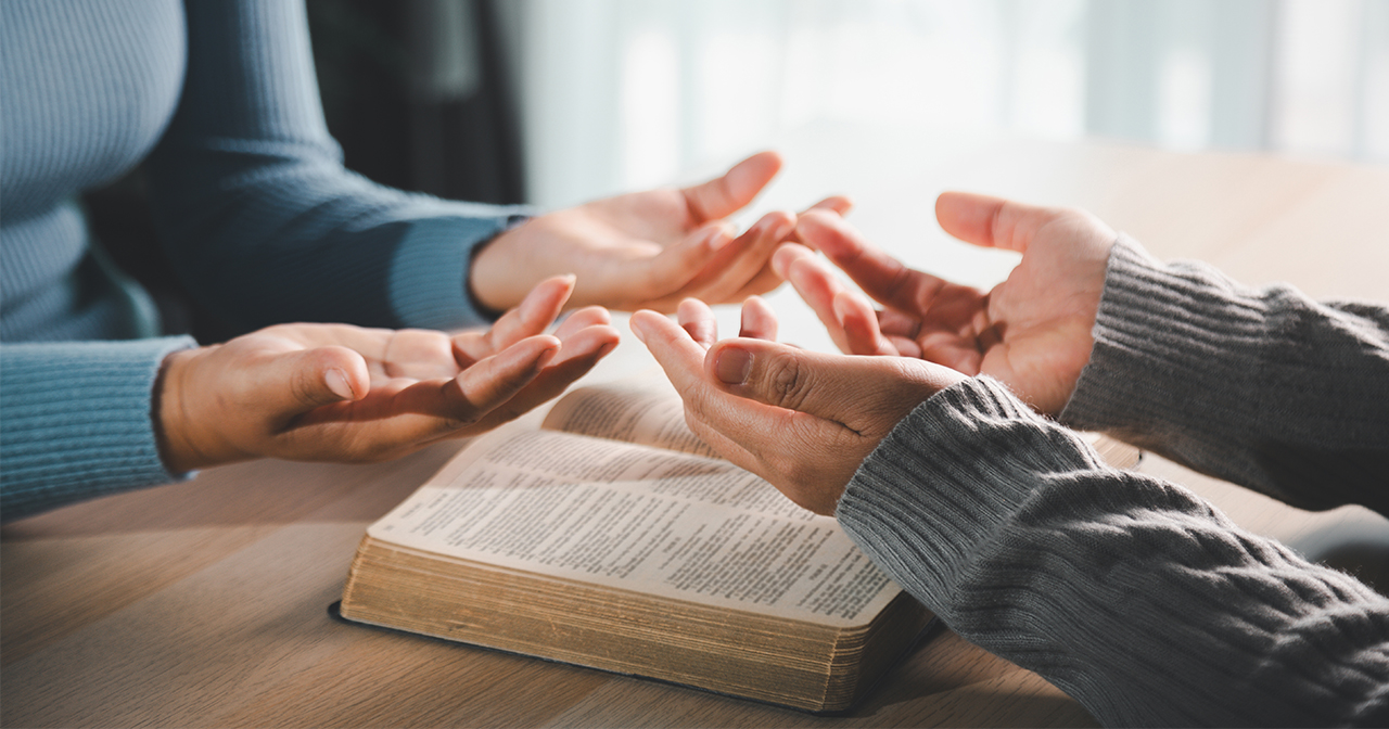 Two people with an open Bible and hands raised in prayer.