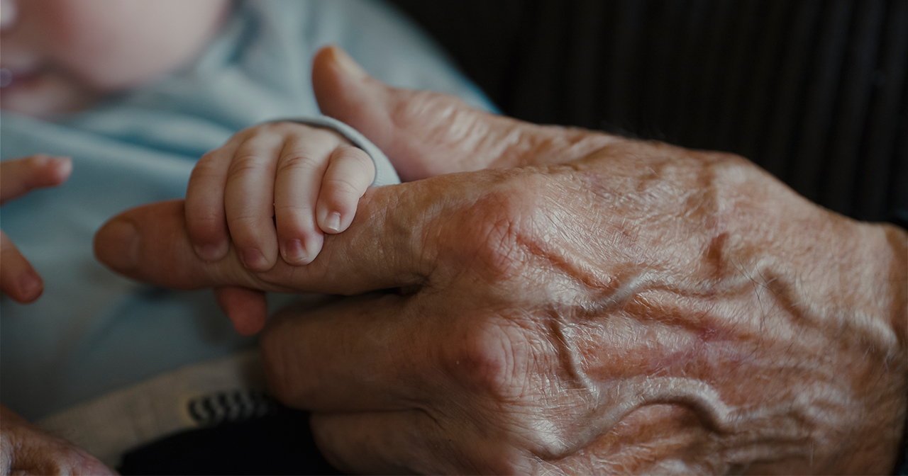 Grandfather gently holding his newborn grandchild's hand.