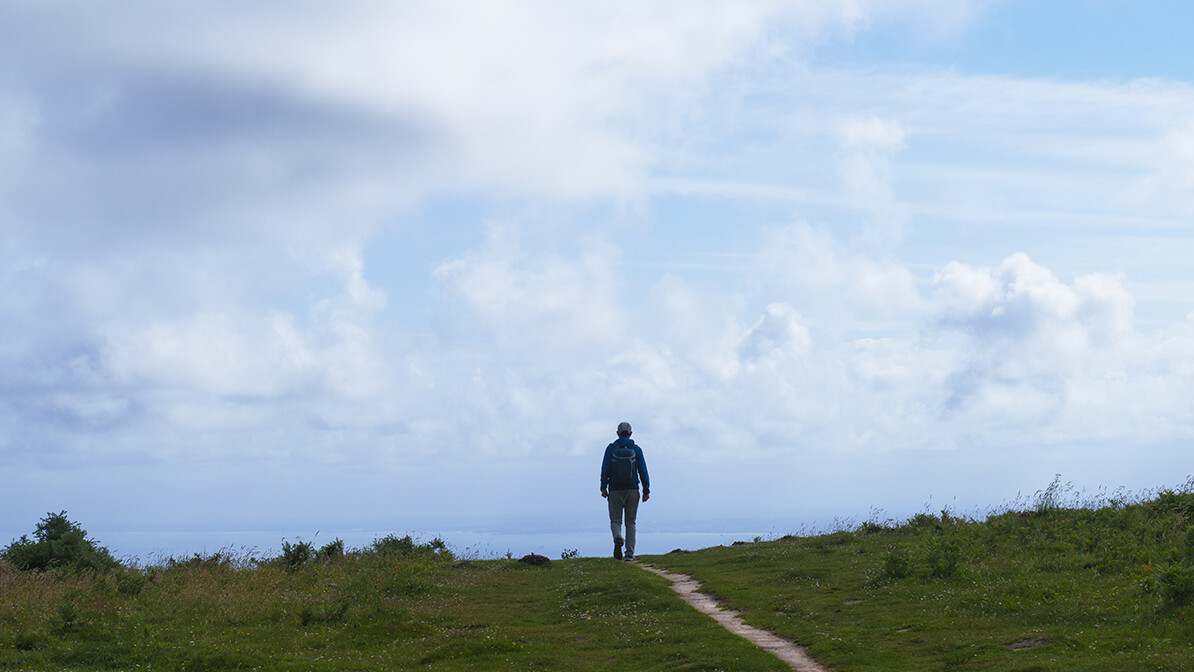 Man walking along a path on a cloudy day.