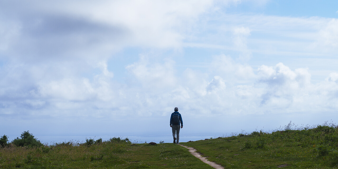 Man walking along a path on a cloudy day.