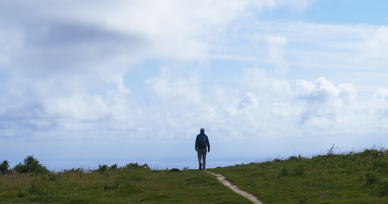 Man walking along a path on a cloudy day.