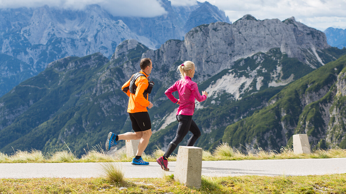 Man and woman running uphill on a trail beside mountains.