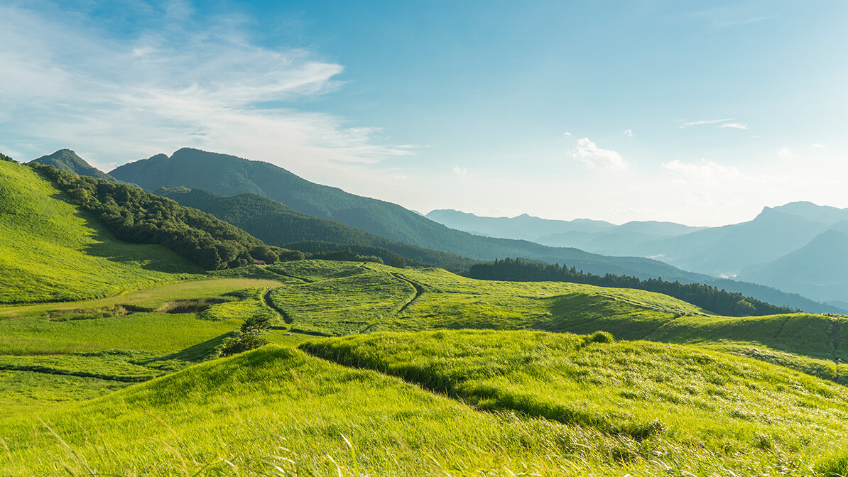 Green valley with mountains in the distance beneath a cloudy sky.