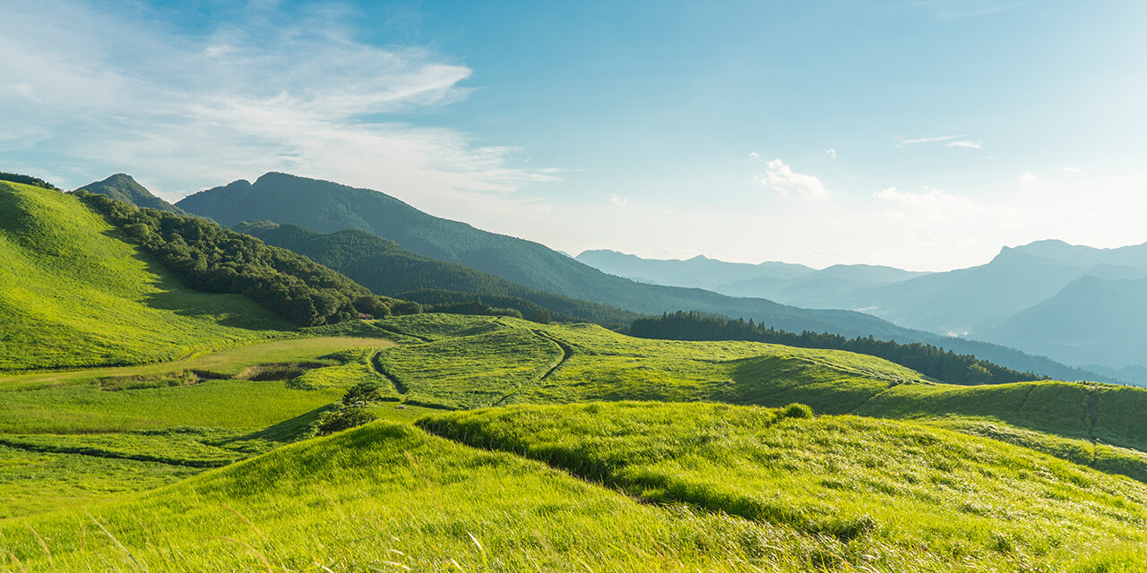 Green valley with mountains in the distance beneath a cloudy sky.