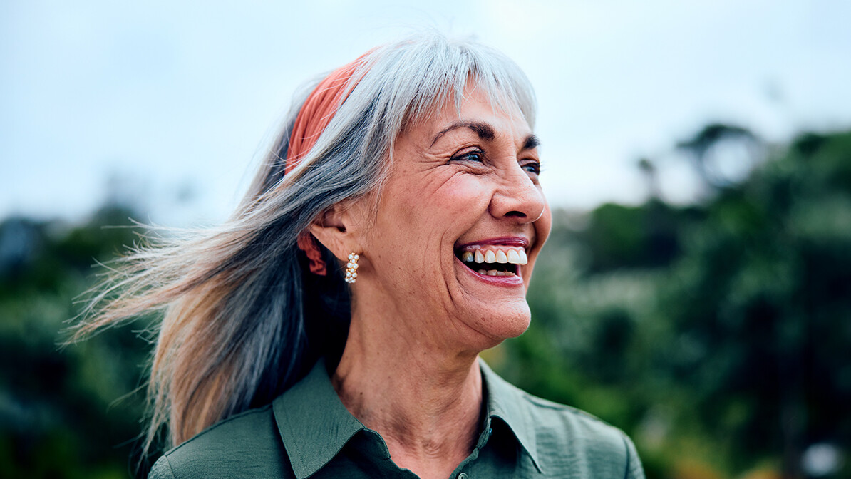 Woman smiling and looking into the distance outdoors with her hair pushed back.