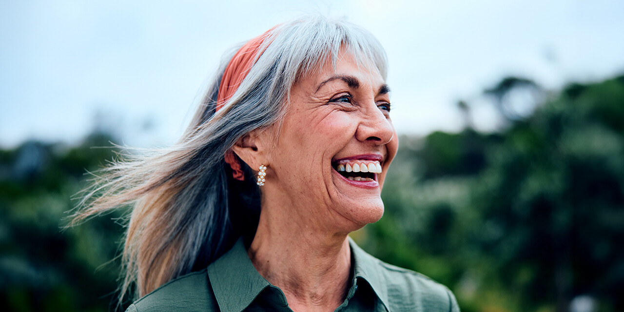 Woman smiling and looking into the distance outdoors with her hair pushed back.