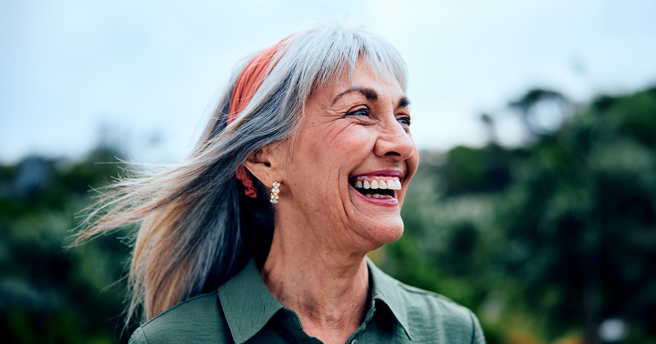 Woman smiling and looking into the distance outdoors with her hair pushed back.