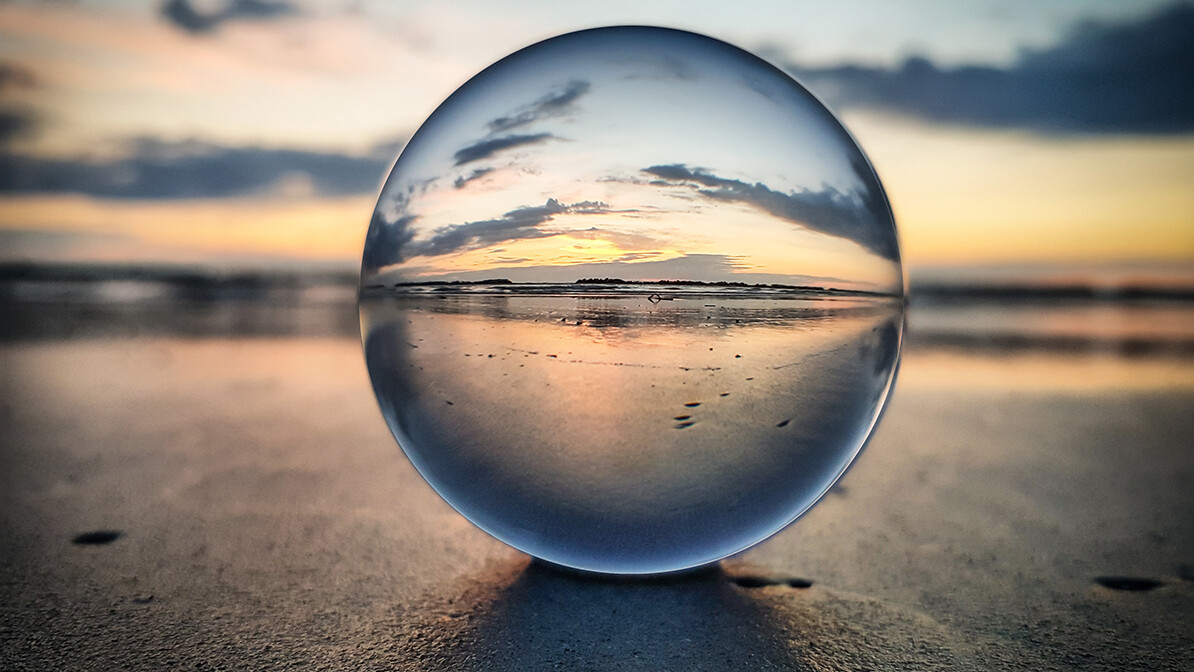 Glass ball resting on a beach, reflecting the sunrise.