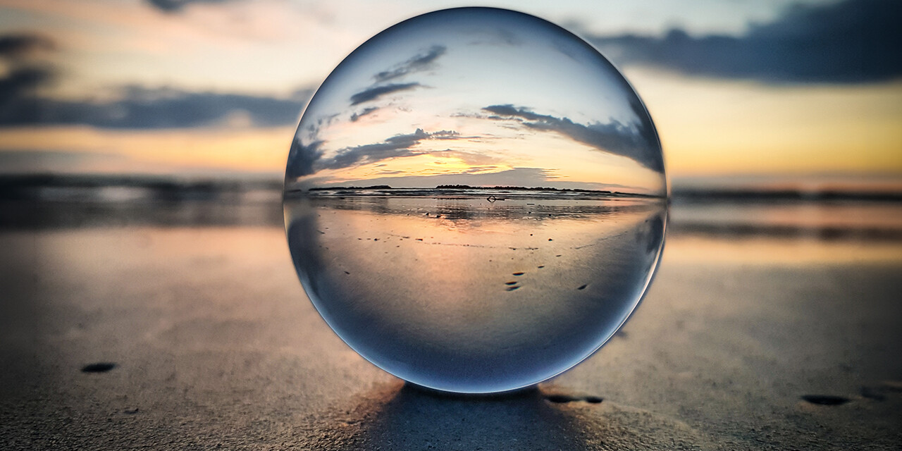 Glass ball resting on a beach, reflecting the sunrise.
