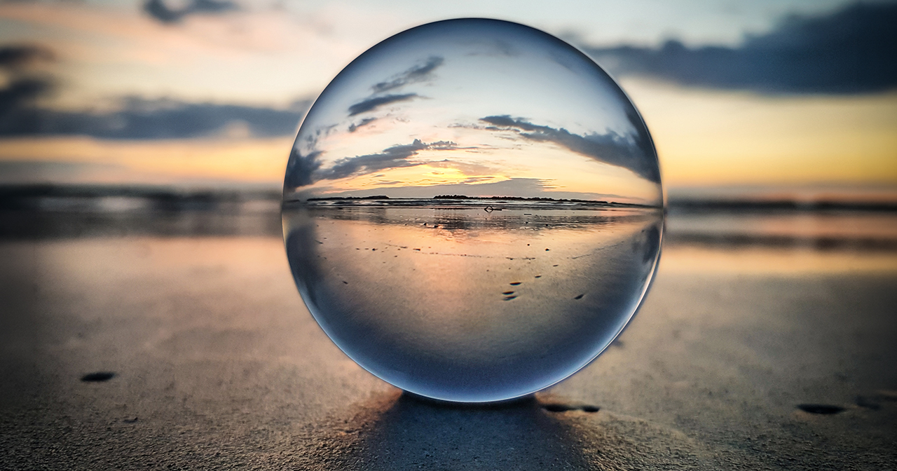 Glass ball resting on a beach, reflecting the sunrise.