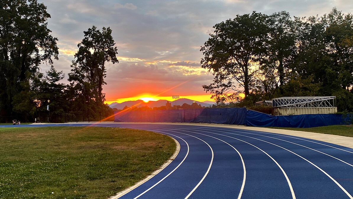 Blue running track at sunset with mountains in the distance.
