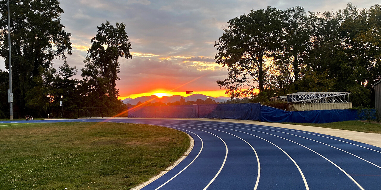 Blue running track at sunset with mountains in the distance.