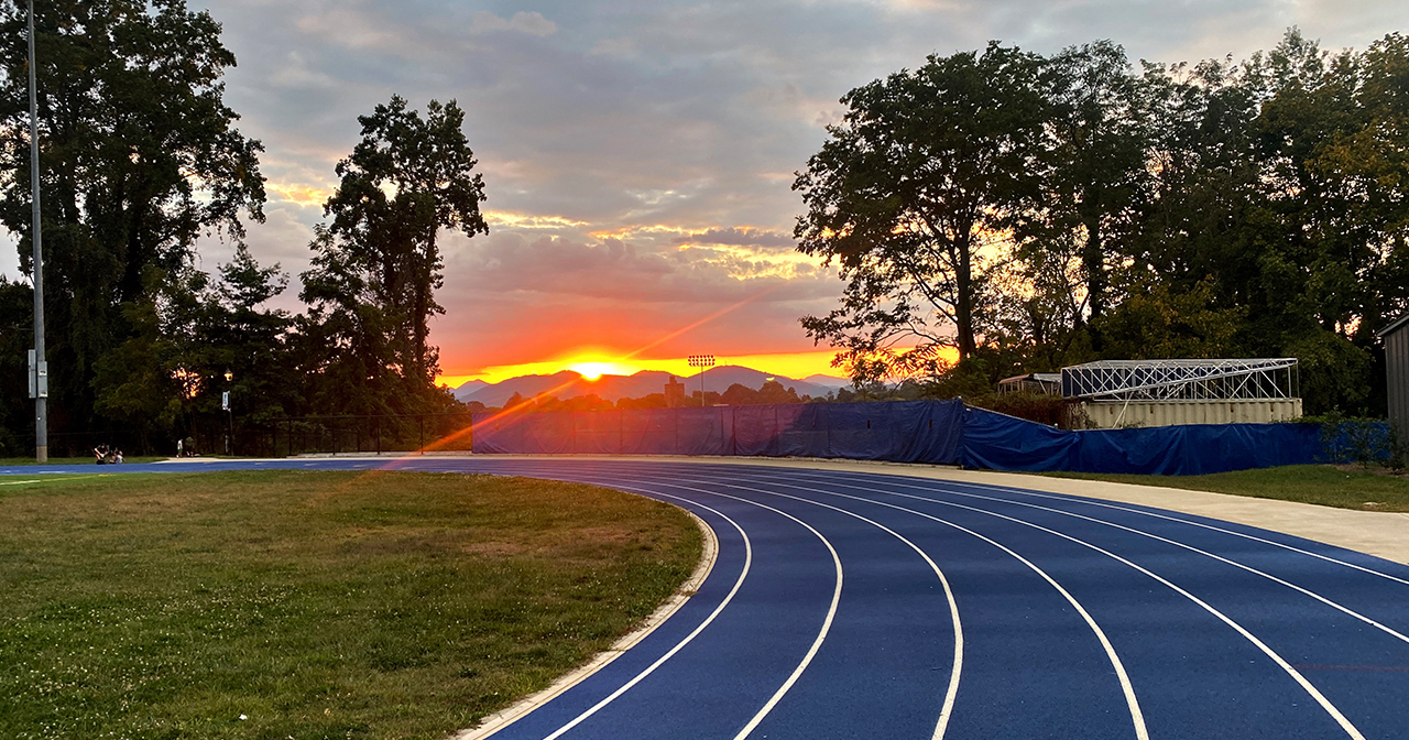 Blue running track at sunset with mountains in the distance.