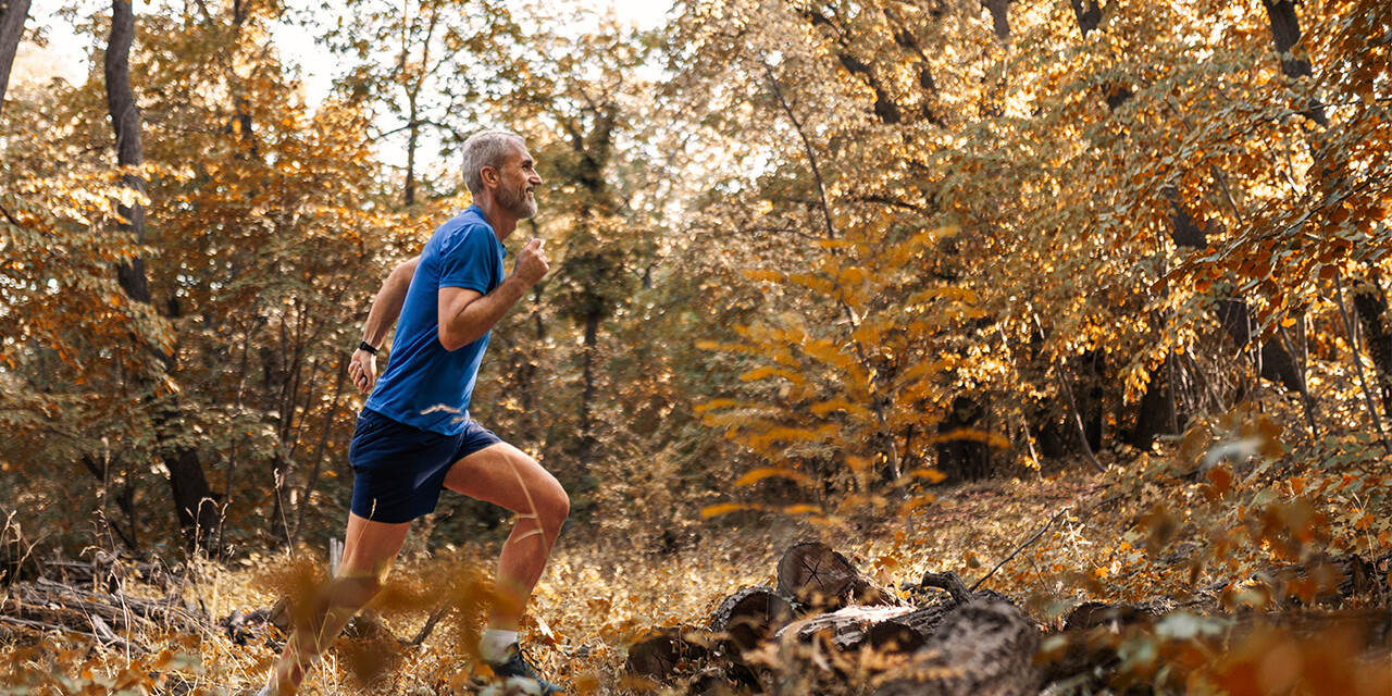 Man running along a forest trail with colorful fall leaves.