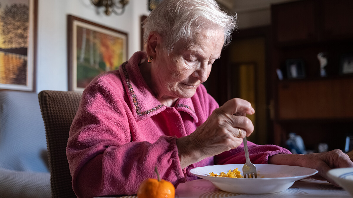 Elderly woman smiling at the table with a bowl of pasta