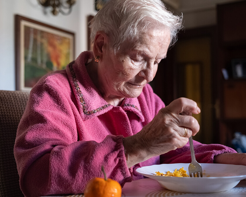 Elderly woman smiling at the table with a bowl of pasta