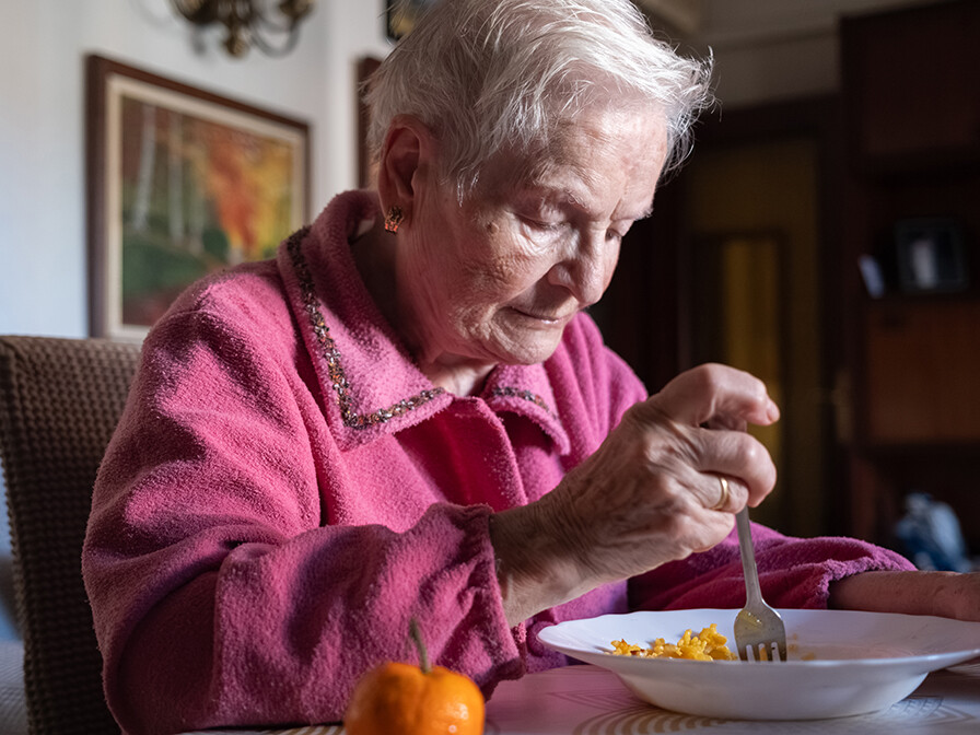 Elderly woman smiling at the table with a bowl of pasta